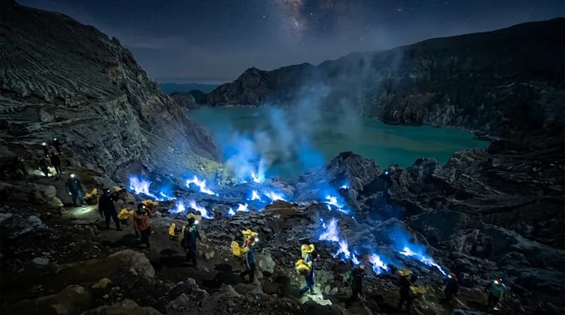 Blue fire Kawah Ijen Banyuwangi dengan api biru menyala di kegelapan dan danau asam di latar belakang